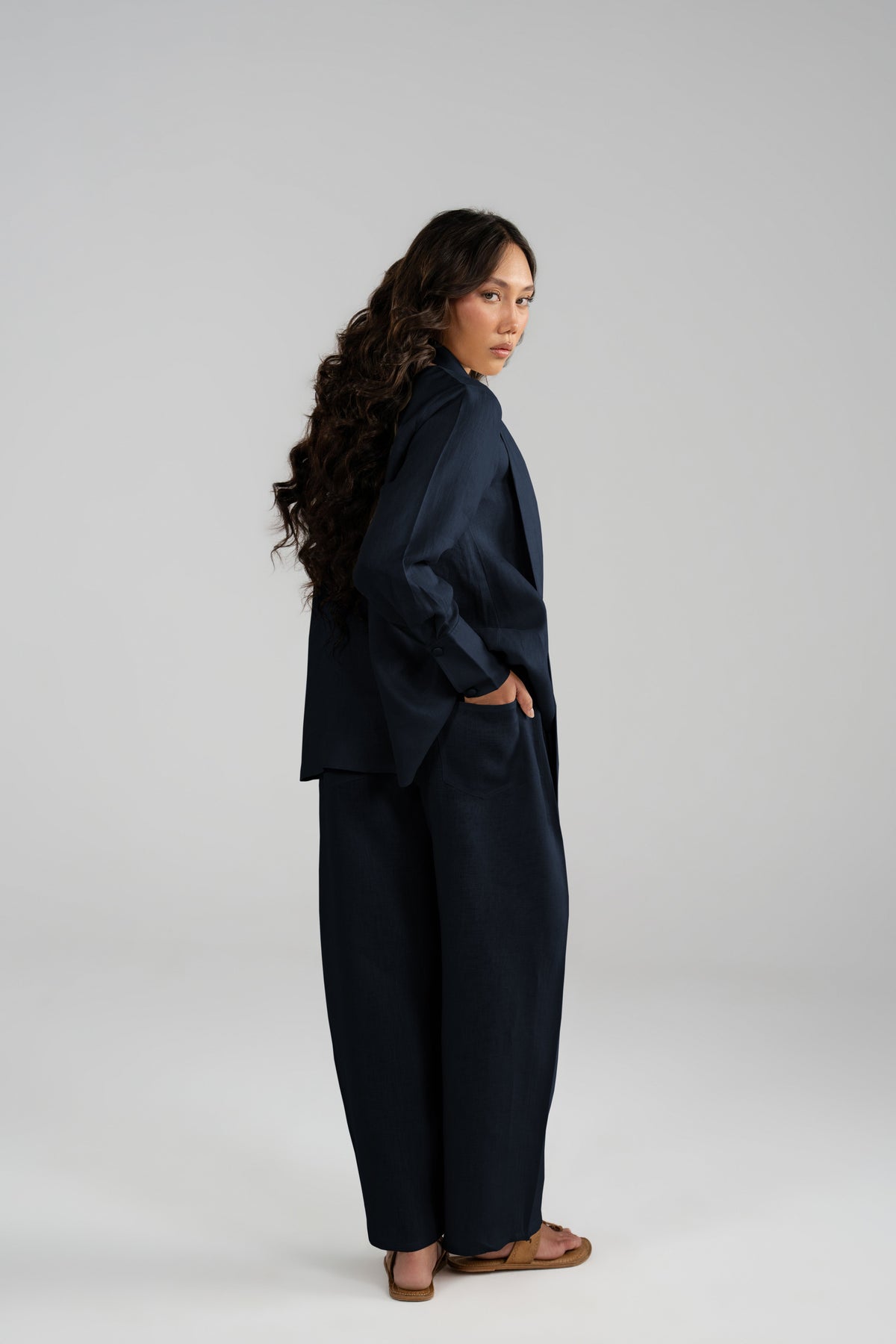 Side profile view of a woman wearing the Cove Set in navy blue pure linen, showing the drape of the short scarf and wide-leg balloon trousers.