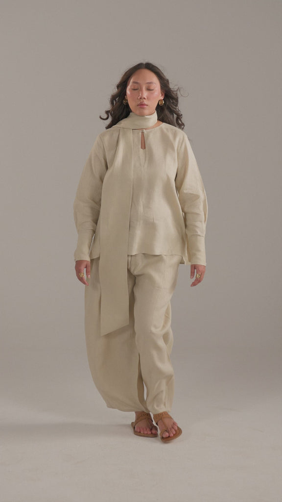 Model walking in the Tuscany Set, beige linen three-piece with balloon trousers, with having scarf in motion